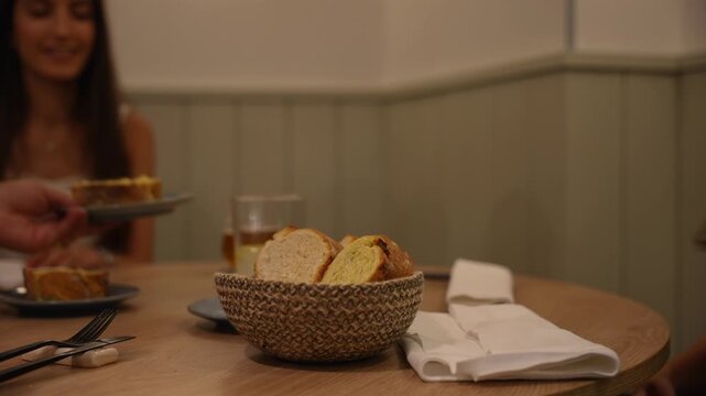 Person serving a slice of bread at a dinner table inside a restaurant. Slowmo