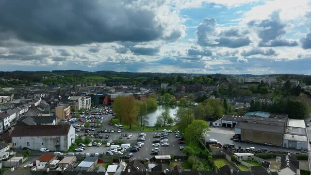 Monaghan Town, County Monaghan, Ireland, April 2024. Drone ascends over apartment buildings to parking lot with Patena Lake at city center in below overcast cloudy sky.