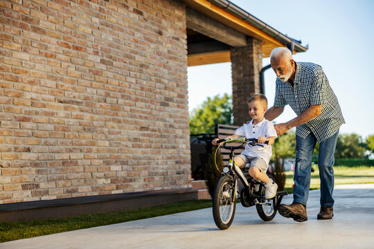 Caring grandfather is helping his grandson to learn riding a bicycle.