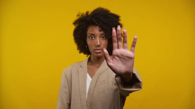 Woman Gesturing Stop with Hand Against Yellow Background