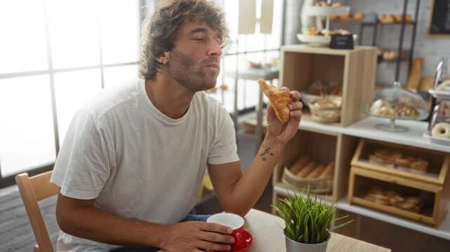 Young man enjoying a croissant in a cozy bakery with indoor seating and various pastries in the background