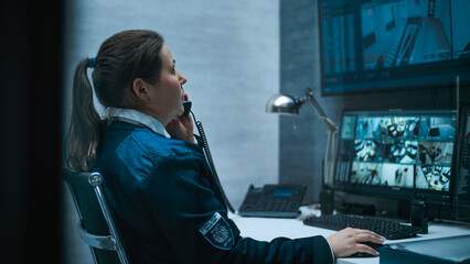 Female security worker or dispatch works on computer in monitoring center with CCTV cameras, talks...