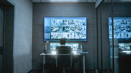 African American CCTV operator works with security cameras on computer and tablet in dim monitoring...