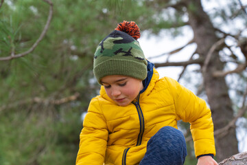 Portrait of little boy playing in a forest wearing warm clothes and a woolen hat