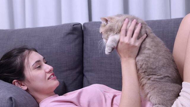 Young Woman Relaxing on Sofa While Holding and Gazing Lovingly at Her Cat, Bonding and Enjoying Quality Time Together in a Cozy Home Environment