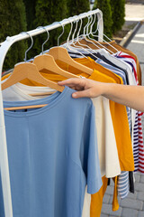 female hand holding a hanger with a t-shirt. clothes of different colors on a hanger. t-shirts, long sleeves. Sale of clothes. fashion. Shopping.  choice of clothes.