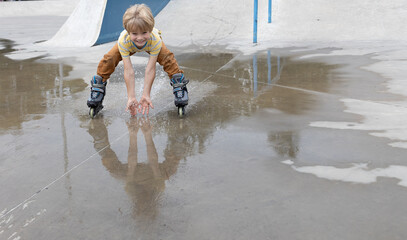 boy joyfully rides at speed on roller skates through a puddle after the rain, making splashes with...