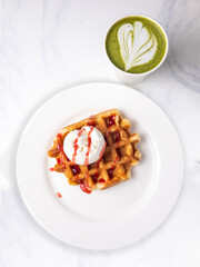Belgian waffles with ice cream and strawberry sauce on white plate