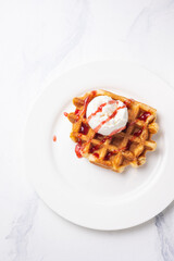 Belgian waffles with ice cream and strawberry sauce on white plate