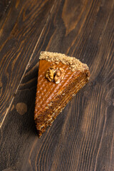 A piece of cake with walnuts on a dark wooden background.