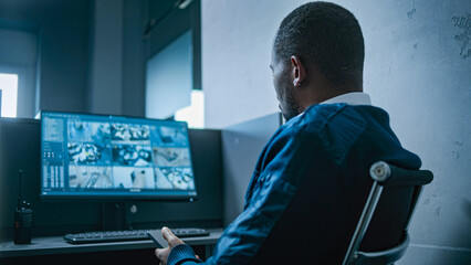 African American male security guard uses mobile phone sitting at the workplace in the office....