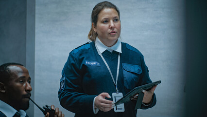 Female security worker talks with African American male colleague, uses tablet computer. Multiethnic surveillance operators control security cameras working in modern monitoring center. CCTV system.