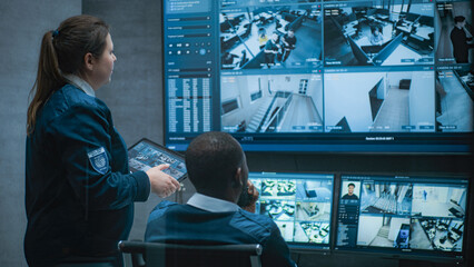 Female security worker talks with African American colleague, uses tablet. Multiethnic CCTV...