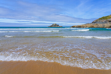 Waves wash up Crantock beach on a bright summer morning.