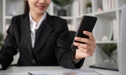 Young Female Accountant Sitting at Desk Doing Paperwork and Using Smartphone in Modern Office