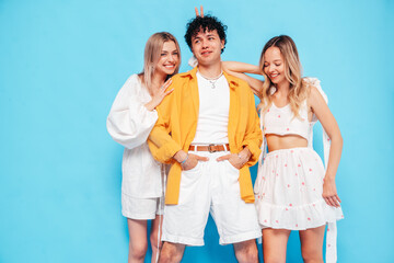 Fototapeta premium Group of young three stylish friends posing in studio. Fashion man and two cute female dressed in casual summer clothes. Smiling models having fun. Cheerful women and guy near blue wall