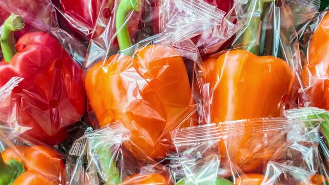 Horizontal pan over fresh plastic wrapped orange and red bell peppers
