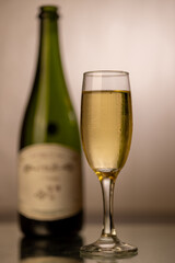 Detailed shot of a cold champagne flute with a green champagne bottle blurred to the right. The vertical image features a luxurious gold gradient background