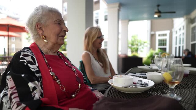 Mature woman and elderly woman or grandmother sit at outdoor cafe smiling and laughing.