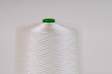 Close-up of a white spool of braided fiberglass thread with a green cap, isolated on a light background. Industrial and manufacturing material concept.