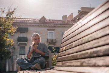 A woman sitting on a bench with a cell phone in her hand. She is wearing a suit and she is working on her phone.