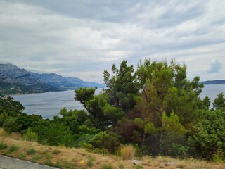 Scenic landscape of  mountains and sea on a cloudy summer day. People hurry up to vacation on of beautiful clean place by the Adriatic Sea. View of the coast of rocky island. Curve road in mountain.