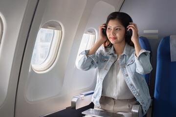 Young Business Woman Traveling by Plane, Wearing Headphones and Sitting by Window, Enjoying In-Flight Entertainment