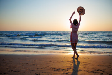girl dancing on the beach. Attractive happy young woman in dress and hat enjoying free time at sunset outdoors.
