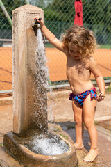 pretty portrait of a 2 year old girl with curly blonde hair playing with water from a fountain