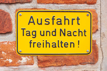 Gelbes Schild Ausfahrt Tag und Nacht freihalten an einer rötlichen Backsteinmauer, Deutschland
