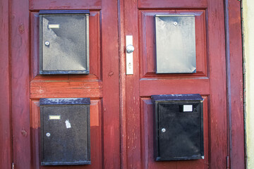 An exterior red wooden door of a residential building with multiple small square glass panes and four old mail boxes