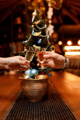 small, beautiful girl and a handsome man are holding two glasses of delicious champagne in front of a Christmas tree in a cozy, charming restaurant