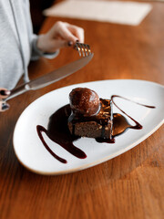 delicious dessert with black sponge cake, covered in chocolate cream, and white ice cream, served on a beautiful white plate on a wooden table in a cozy, charming restaurant
