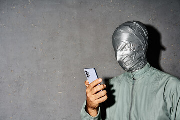 Mystery man with duct tape face types text message on cell phone, enjoys online communication