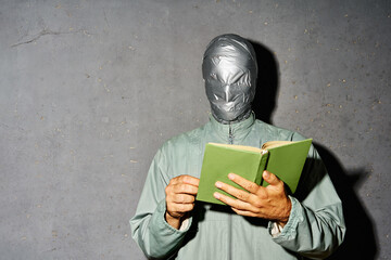 Mystery man with duct tape face relax and reading book over gray background