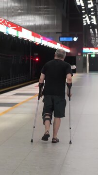 Mature man with bondage, medical splint, knee brace on the leg going to the subway using crutches. Accessible urban environment for the disabled, recovery from injury.
