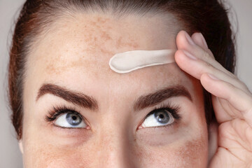 Caucasian woman's face with freckles or age spots, melasma , she smears cream on her forehead with...