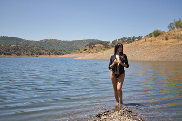Woman, young, beautiful, Latina, brunette, with a golden crown, black shirt and bikini, as if she were a goddess of water, coming out of the middle of a lake. Concept beauty, water, myths, legends.