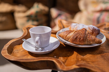 Morning coffee with croissant and espresso on a unique wooden table. Croissant, french traditional pastry on a white plate. Selective focus.	
