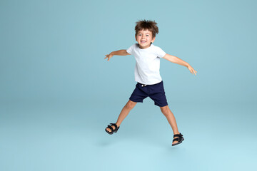 A little funny boy jumping up, enjoying time, over blue background. Copy space.