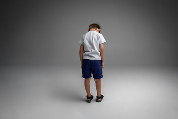 Back image of a single little boy sit with head down, isolated grey background.