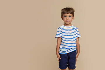 Front portrait of a little boy with blue eyes, dressed in a t-shirt with lines, looking at camera, over beige background. Copy space.