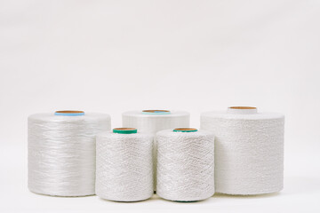 A group of five spools of white fiberglass yarn in different sizes and textures, arranged in a row against a plain white background.