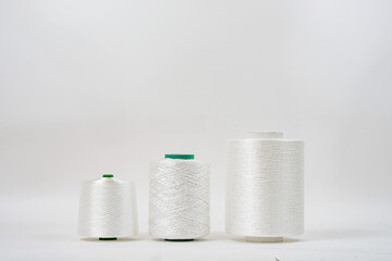  Three spools of white fiberglass yarn in different sizes are aligned in a row against a plain background, showcasing their texture and form.