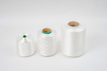 Three spools of white fiberglass yarn in different sizes are aligned in a row against a plain white background, showcasing their texture and form.