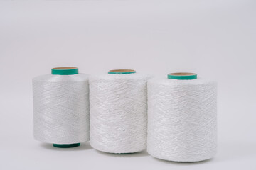 Three large spools of white fiberglass thread are arranged in a row, each displaying a different texture and weave pattern on a plain background.