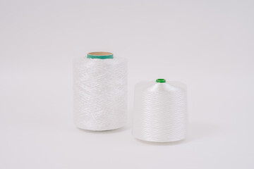  Two spools of white fiberglass thread, one taller with a green core and the other shorter with a green tip, placed on a white background.