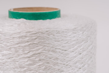 Close-up of a spool of braided fiberglass threads with a green core, showcasing the intricate texture and weave of the material.