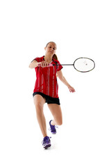 Young athletic woman playing badminton, in motion leaping to hit shuttlecock, attacking opponent against white studio background. Concept of individual sport, tournament, match, championship. Ad