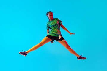 Obraz premium Impressive movement of female badminton player hitting shuttlecock in neon light against gradient blue background. Concept of individual sport, tournament, match, championship. Ad